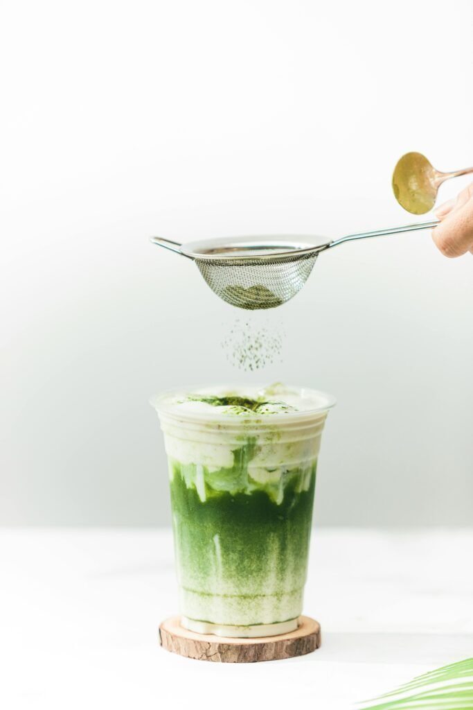 Delicious green matcha latte with milk froth in a clear disposable cup, styled with matcha powder.